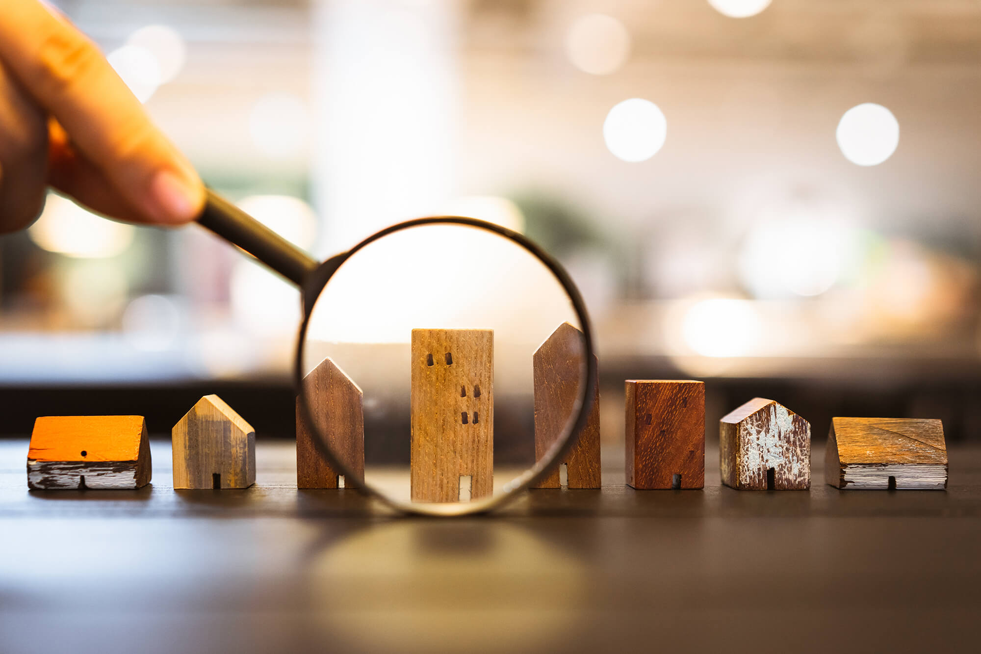 Hand holding magnifying glass and looking at house model